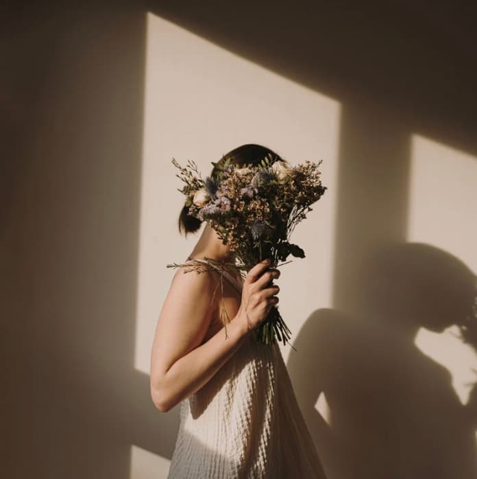Femme tenant un bouquet de fleurs séchées devant son visage, dans une lumière rasante