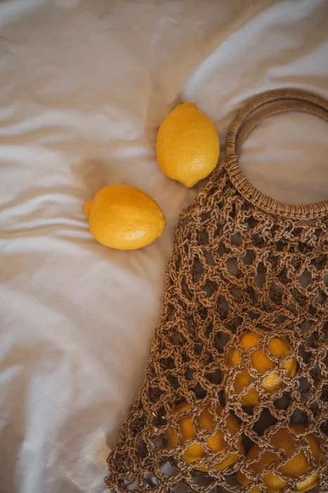 Deux citrons et un filet à provisions en jute posés sur un drap de lin froissé