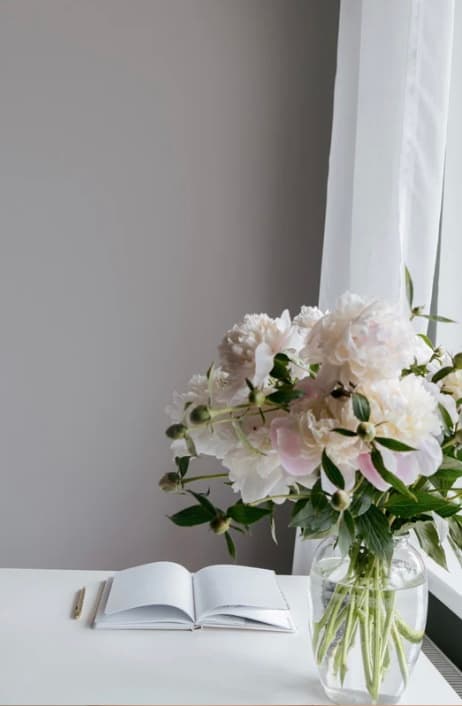 Bouquet de pivoines blanches et carnet ouvert sur un bureau clair, près d'une fenêtre
